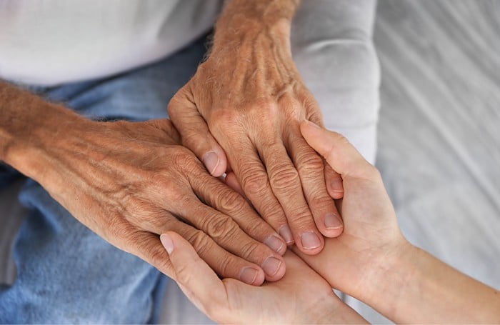 Aide à domicile qui tient les mains d'un senior